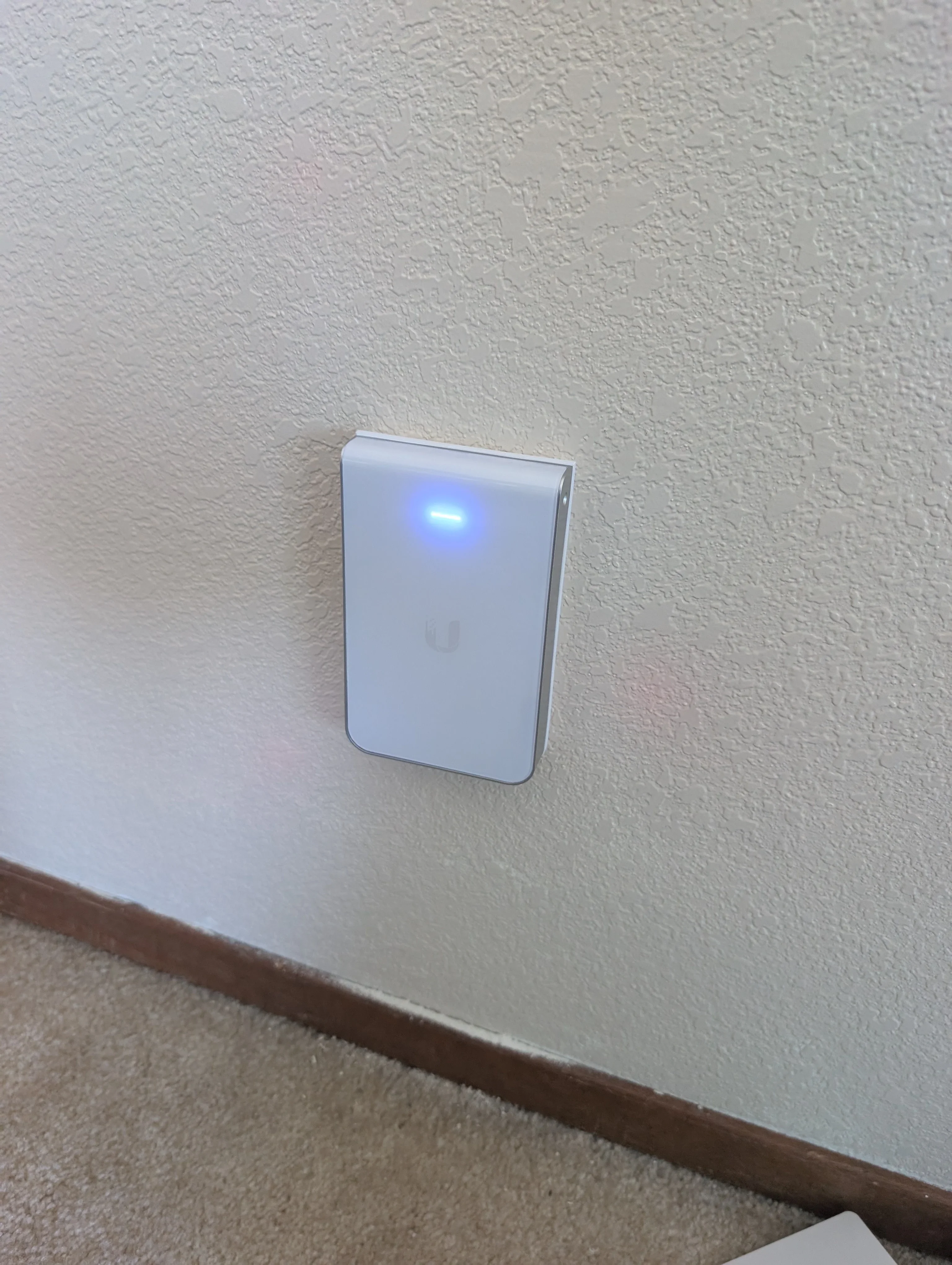 White wireless access point mounted on textured wall with blue LED indicator lit