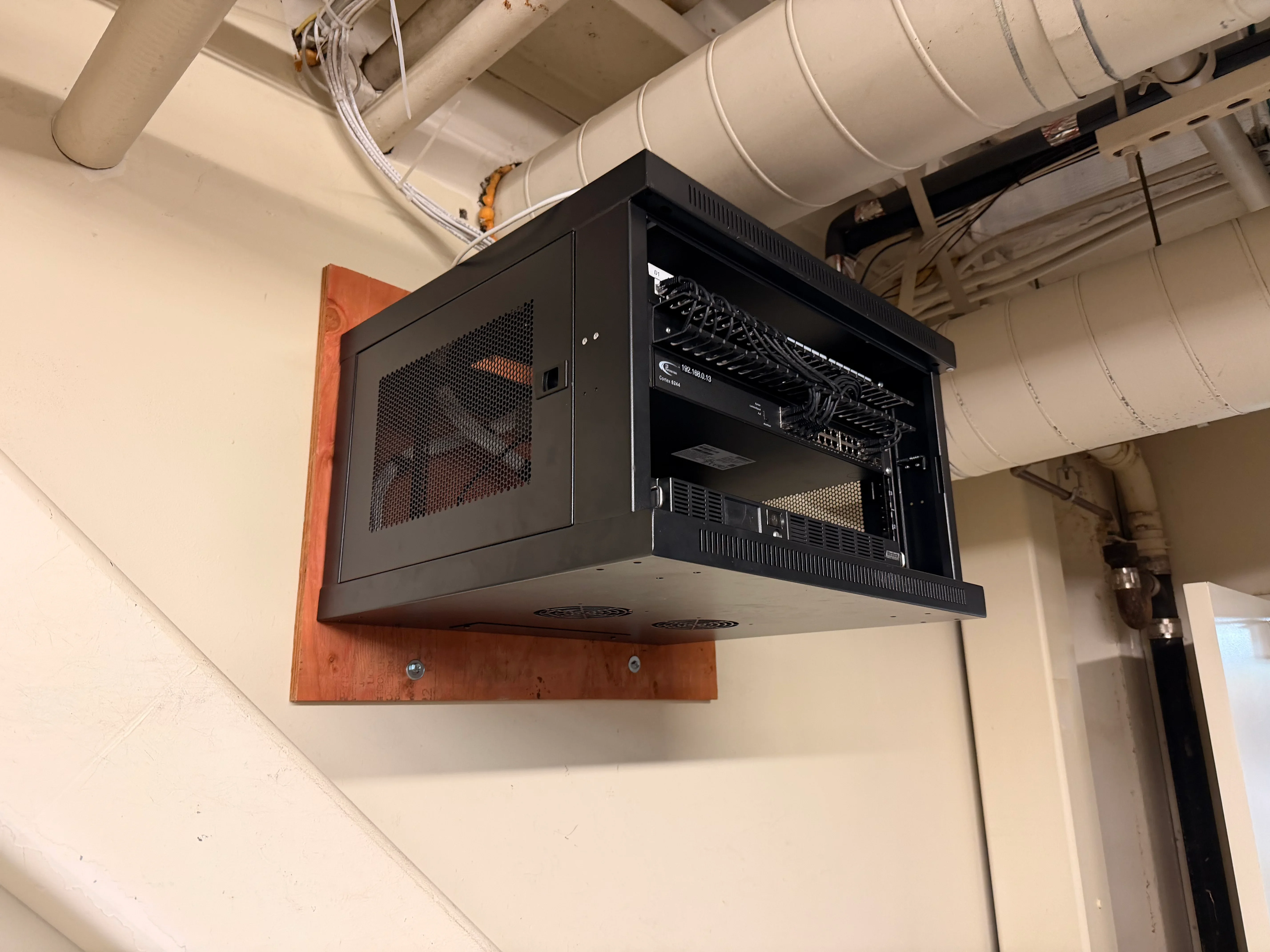 Black wall-mounted network rack with patch panels and organized cabling in commercial space