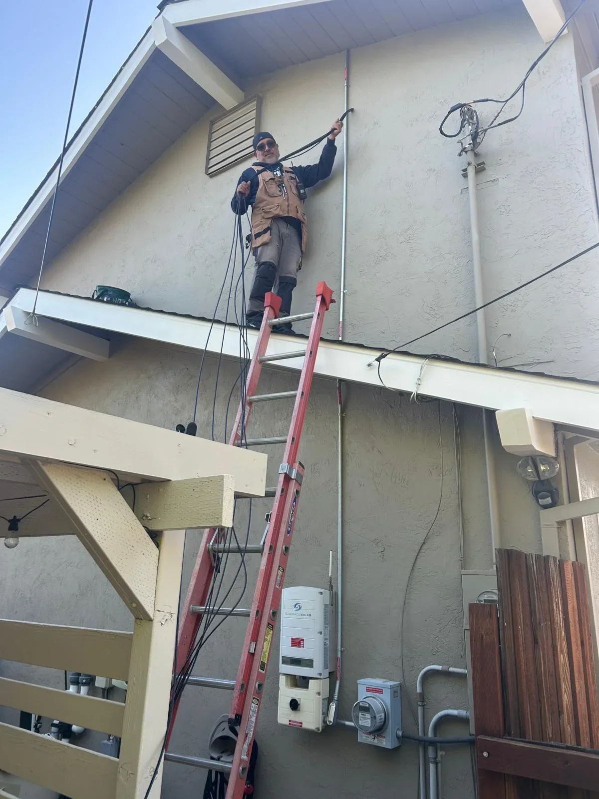 Technician on ladder installing telecommunications equipment on residential building exterior