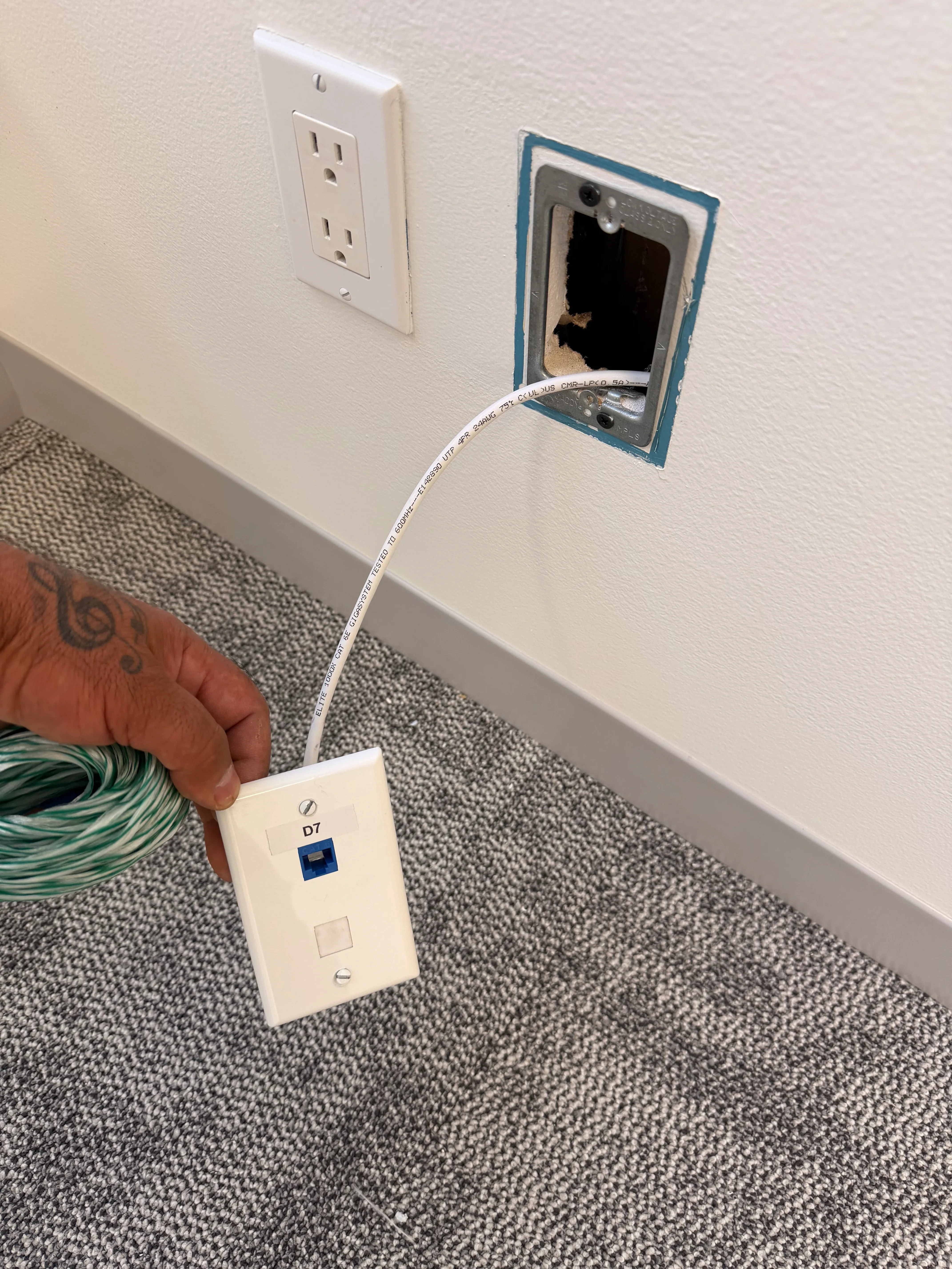Network cable installation with white data cable routed to blue wall outlet box next to standard electrical outlet